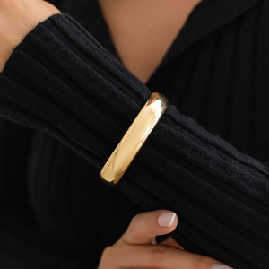 Close-up of golden liquid metal spring bracelet on black ribbed knit sleeve texture