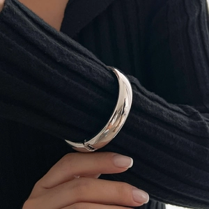Polished silver liquid metal spring bangle on a black knit sleeve for a minimalist look