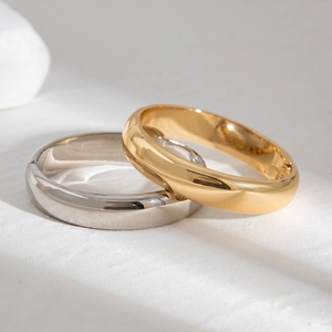 Detailed view of wide polished gold and silver hinge bracelets on a textured background