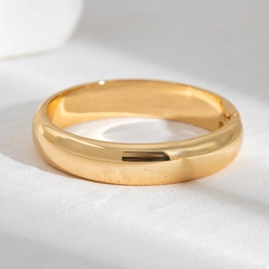 Close-up of polished gold-tone wide bangle bracelet with hinged clasp detail