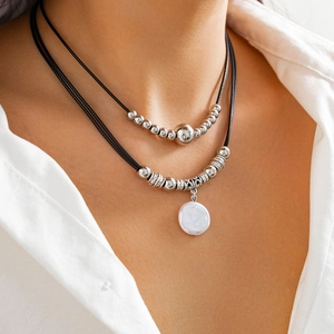 Detail of layered necklace featuring silver metal beads and a white shell disc pendant