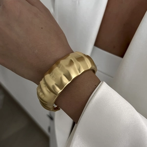 Close-up of wide golden cuff bracelet featuring vertical pleated texture on model wrist