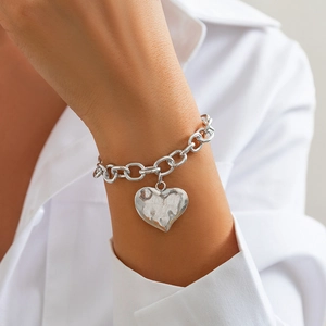 Dettaglio di un bracciale a catena d'argento con ciondolo a cuore martellato sul polso