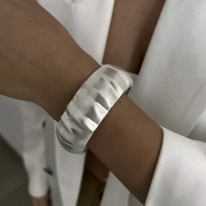 Detail of wide silver bangle featuring wavy brushed texture and minimalist matte finish