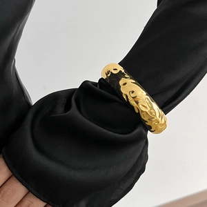 Macro view of textured liquid metal gold cuff bracelet over elegant black silk sleeve
