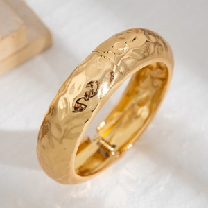 Detail of wide golden hammered metal cuff bracelet with liquid texture and spring hinge