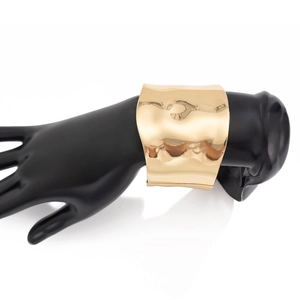 Close-up of a wide gold cuff bracelet featuring irregular hammered texture on a hand model