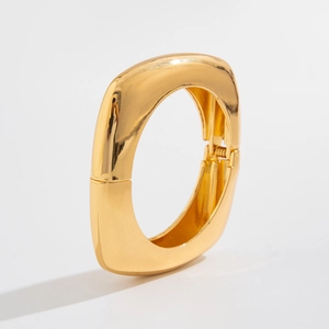 Detail of chunky gold hinged bracelet with high-polish mirror finish on white background