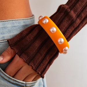 Primer plano de un brazalete ancho de resina naranja con perlas sobre una manga tejida