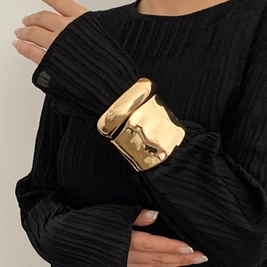 Minimalist wide gold bangle with irregular pleated metal texture worn by a model