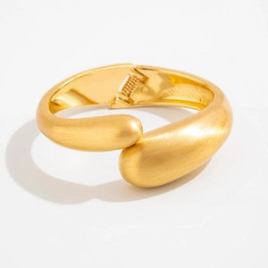Detail of matte gold water drop bangle with textured finish and hidden hinge closure