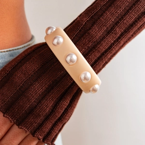 Primer plano de brazalete ancho de resina crema con perlas sobre una manga de punto marrón