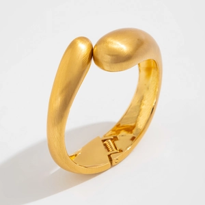 Macro shot of the spring hinge detail and brushed gold finish on the wide metal bangle