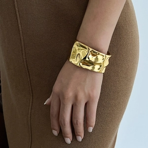 Macro detail of wide gold liquid metal bracelet with irregular pleated texture on wrist