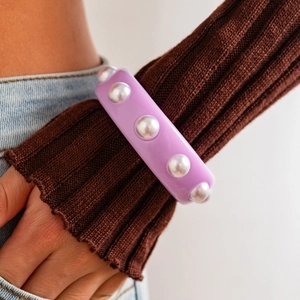 Detalle de brazalete ancho de resina morada con cinco perlas de imitación sobre un suéter