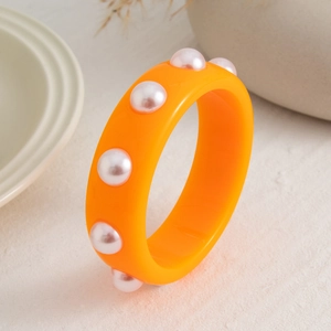 Detalle de brazalete ancho de resina naranja con perlas de imitación incrustadas