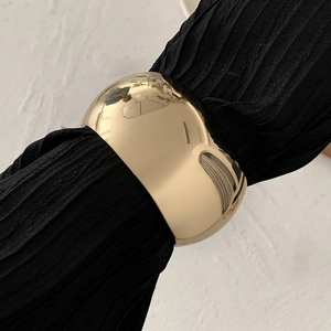 Macro view of gold minimalist chunky wide cuff bracelet against black pleated fabric background