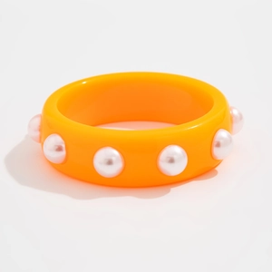 Detalle de brazalete ancho de resina naranja con perlas blancas sobre fondo blanco