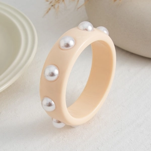 Detalle de brazalete ancho de resina crema con perlas de imitación blancas incrustadas
