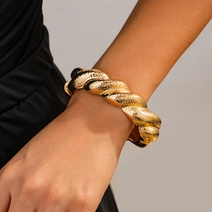 Close-up of a chunky twisted gold bangle with hammered texture on a model wrist