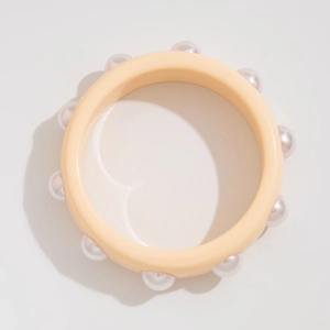 Detalle de brazalete ancho de resina amarillo crema con perlas de imitación incrustadas