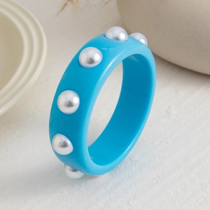 Detalle del brazalete de resina azul cielo con perlas de imitación en fondo neutro