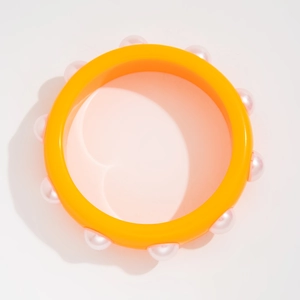 Primer plano de brazalete de resina naranja vibrante con once perlas blancas decorativas