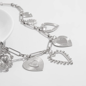 Detail of silver paperclip chain necklace with multiple heart pendants on a white plate