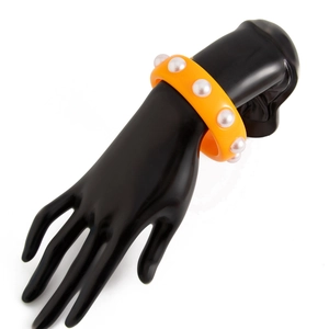 Detalle de brazalete ancho de resina naranja con perlas blancas en soporte de mano negro