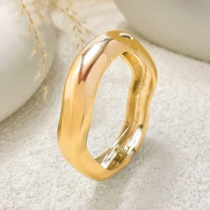 Detail of chunky gold irregular wave bracelet with spring hinge on textured sand