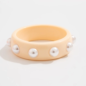 Vista macro del grueso brazalete de resina beige con grandes perlas sobre fondo blanco