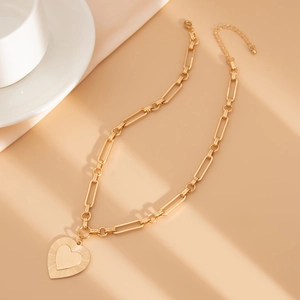 Macro view of gold heart pendant with radial stripe texture on paperclip chain necklace
