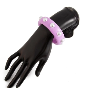 Detalle de una pulsera ancha de resina morada con perlas de imitación sobre un modelo de mano negra