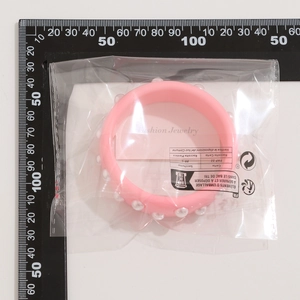 Detalle de brazalete ancho rosa con purpurina y perlas blancas en su empaque original