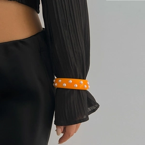 Primer plano de un brazalete ancho de resina naranja con perlas sobre una manga negra plisada