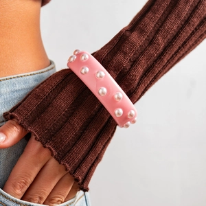 Primer plano de pulsera ancha de resina rosa con perlas blancas en muñeca mujer