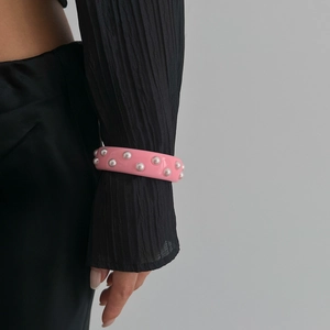 Primer plano de brazalete ancho rosa con purpurina y perlas sobre manga plisada