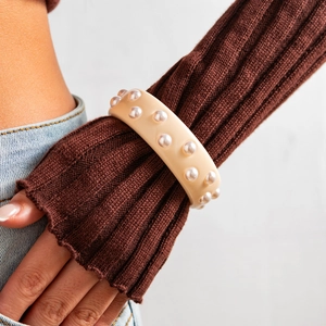 Primer plano de un brazalete ancho de resina crema con dos filas de perlas brillantes