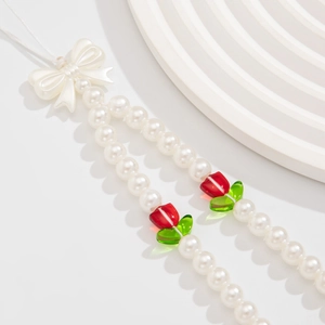 Detail of pearl phone strap with white bow and vibrant red tulip beads on a clean stage