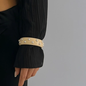 Detalle de un brazalete ancho de resina crema con perlas plateadas incrustadas