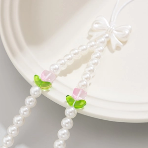 Macro shot of pearl beaded phone charm with white bow and pink tulip floral details