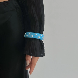 Detalle de brazalete ancho de acrílico azul con cuentas plateadas sobre manga negra