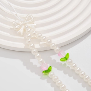 Close-up of pearl phone strap featuring a white bow and pink tulip charms on white stand