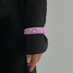 Primer plano del brazalete ancho morado con perlas plateadas sobre una manga negra