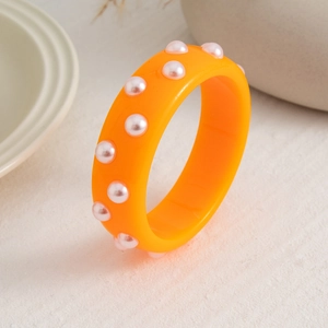 Detalle de brazalete ancho de resina naranja con perlas sobre una superficie de cerámica