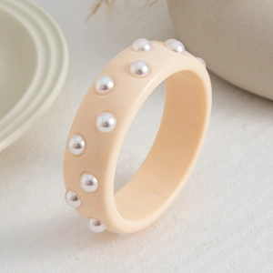 Primer plano de brazalete ancho de resina crema con perlas blancas sobre piedra