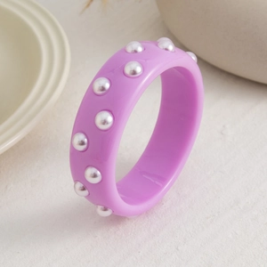 Primer plano del brazalete ancho de resina púrpura con perlas blancas sobre base de piedra