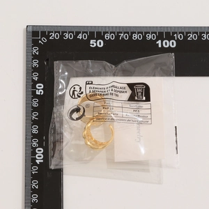 Makroansicht goldener Lava-Ohrringe mit Wellenstruktur in Verpackung mit Skala
