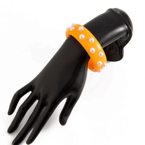 Detalle de brazalete de resina naranja con perlas artificiales en un modelo de mano