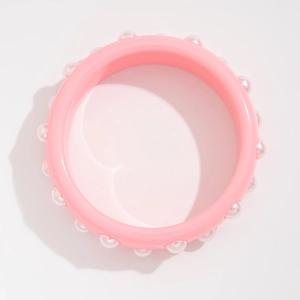 Vista detallada de un brazalete rosa ancho con perlas de imitación blancas y acabado liso